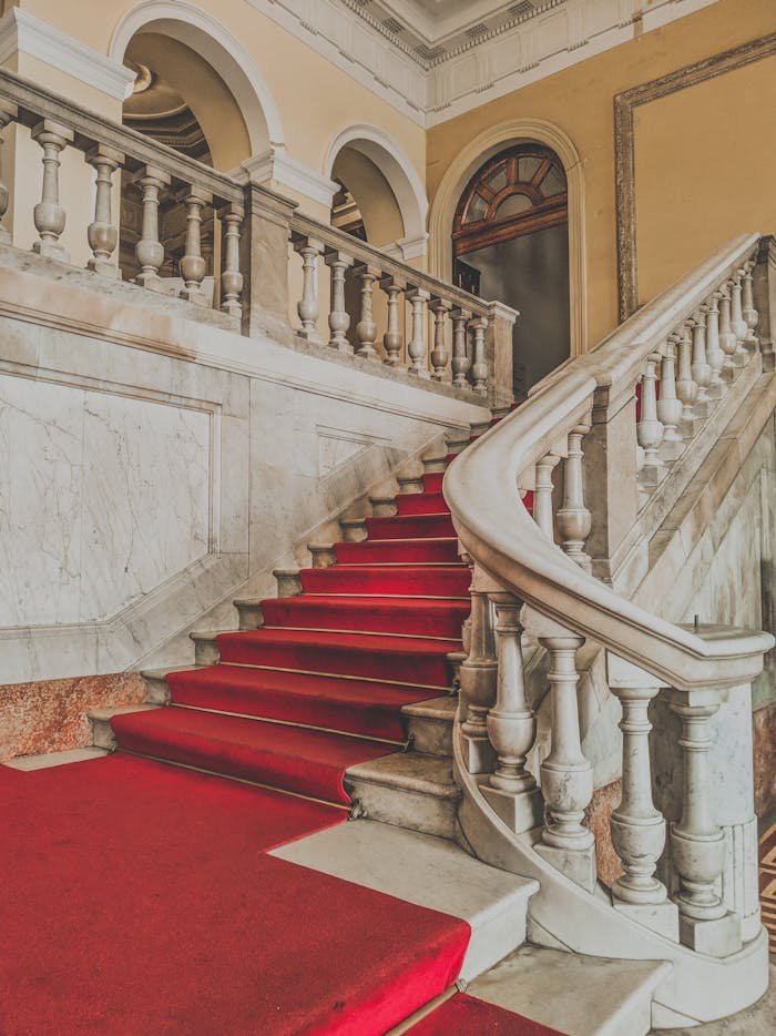 Luxurious interior with a vintage marble staircase and red carpet, embodying grand architectural style.