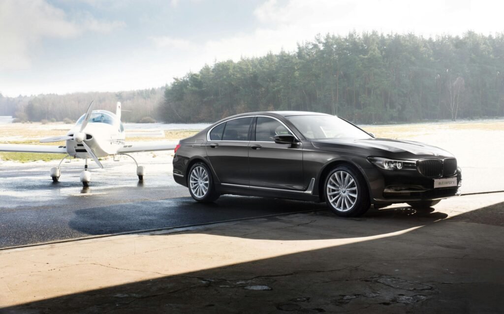 A luxury car parked in front of a small airplane at a sunlit airfield.